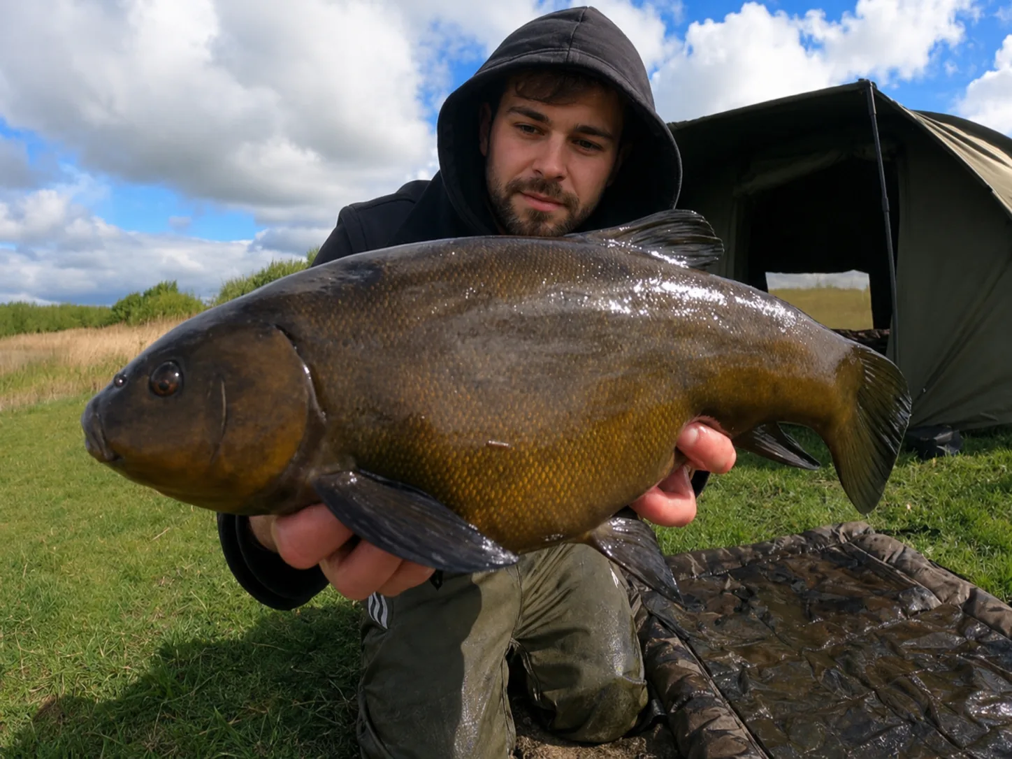 Angler holding a large specimen tench beside an Irish lake.