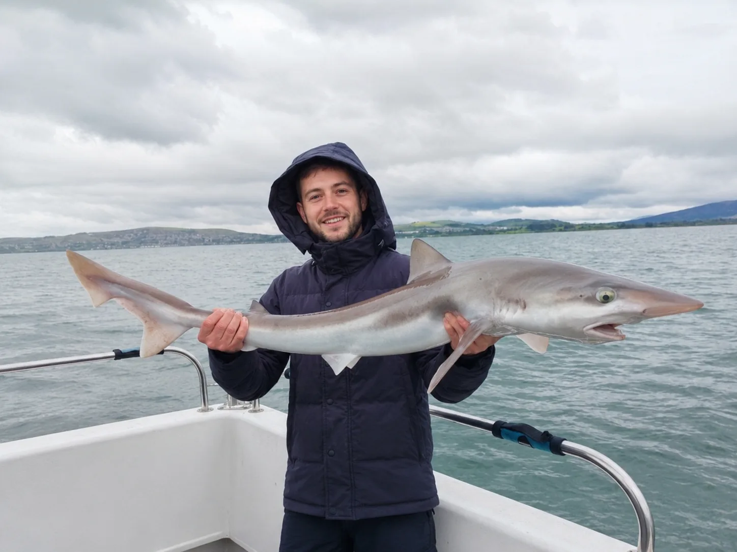 Angler holding a small shark aboard a boat off the Irish coast.